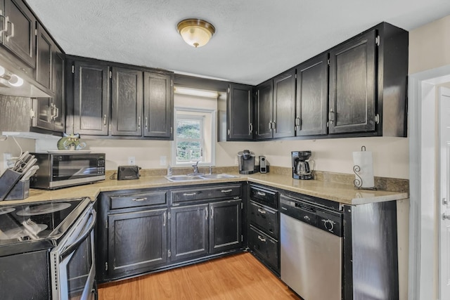 kitchen with ventilation hood, sink, a textured ceiling, light hardwood / wood-style floors, and stainless steel appliances