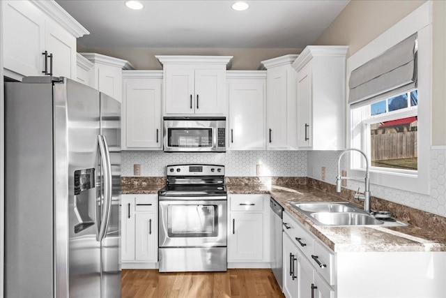 kitchen with sink, stainless steel appliances, tasteful backsplash, white cabinets, and light wood-type flooring