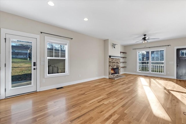 unfurnished living room with a stone fireplace, a wealth of natural light, ceiling fan, and light wood-type flooring