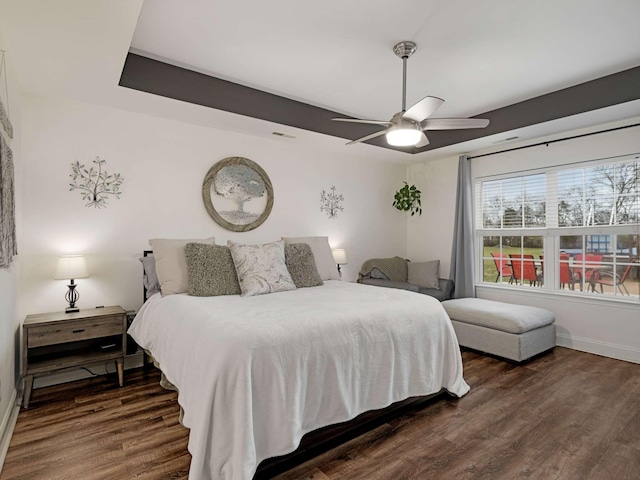 bedroom featuring a raised ceiling, ceiling fan, and dark wood-type flooring