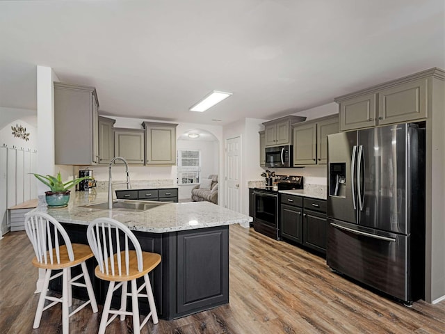 kitchen featuring kitchen peninsula, appliances with stainless steel finishes, gray cabinetry, sink, and hardwood / wood-style flooring