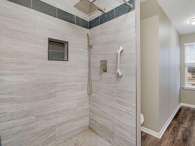 bathroom with toilet, a tile shower, and wood-type flooring