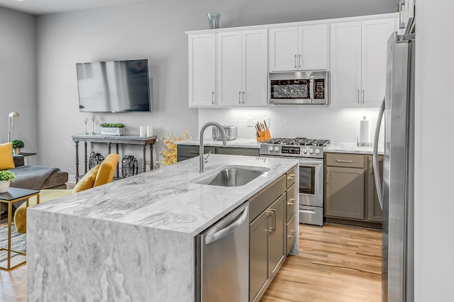 kitchen with a kitchen island with sink, sink, light stone countertops, white cabinetry, and stainless steel appliances