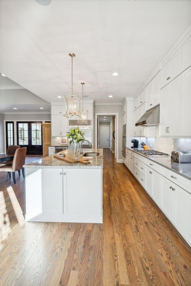 kitchen featuring white cabinets, a large island with sink, hanging light fixtures, and sink