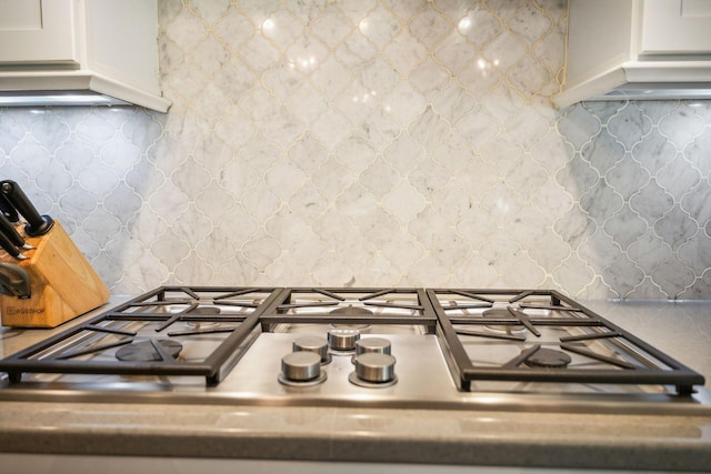 kitchen featuring stainless steel gas stovetop, white cabinetry, and backsplash