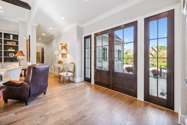 foyer entrance with light hardwood / wood-style floors, crown molding, and french doors