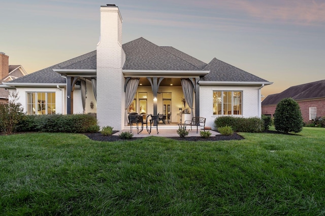 back house at dusk featuring a patio area and a yard