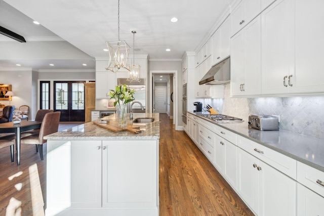 kitchen featuring pendant lighting, backsplash, sink, light stone countertops, and an island with sink