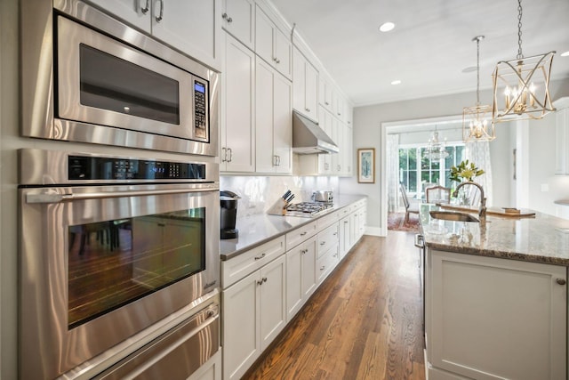 kitchen featuring light stone countertops, appliances with stainless steel finishes, sink, an inviting chandelier, and white cabinetry