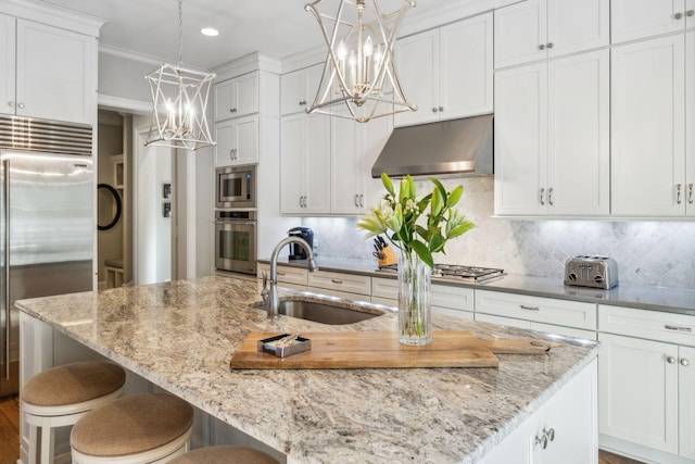 kitchen with built in appliances, decorative light fixtures, sink, and exhaust hood