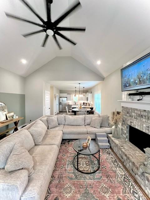 living room featuring ceiling fan, a stone fireplace, and lofted ceiling