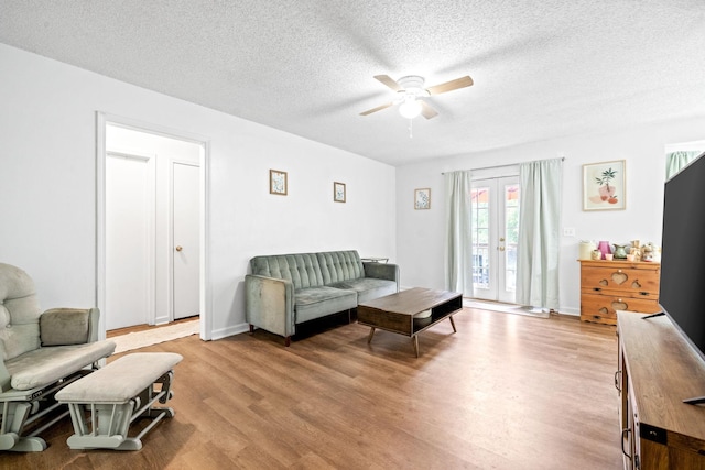 living room with a textured ceiling, ceiling fan, light hardwood / wood-style flooring, and french doors