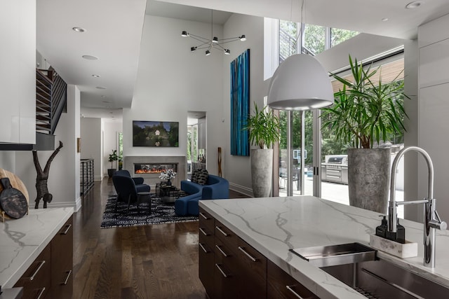 kitchen with dark brown cabinets, light stone counters, a wealth of natural light, and sink