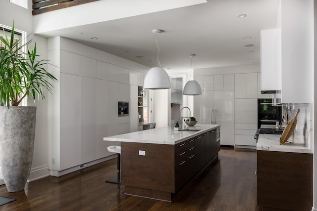 kitchen with dark brown cabinetry, sink, decorative light fixtures, a center island with sink, and white cabinets