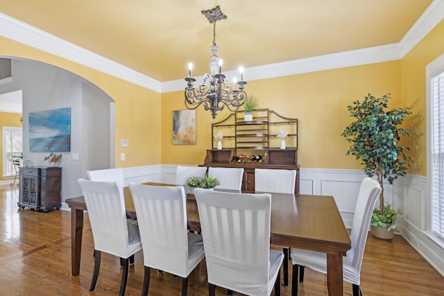 dining room featuring a wealth of natural light, arched walkways, wood finished floors, and wainscoting