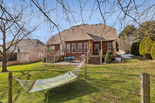 back of property with a patio, brick siding, a yard, roof with shingles, and a wooden deck