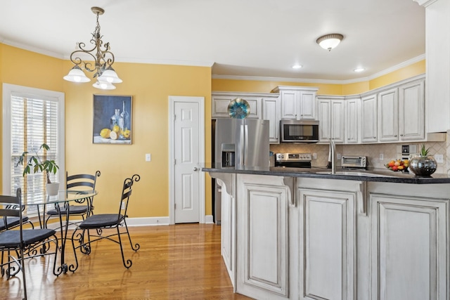 kitchen featuring stainless steel appliances, ornamental molding, light wood-type flooring, and dark countertops