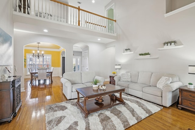 living room with arched walkways, a notable chandelier, a towering ceiling, ornamental molding, and hardwood / wood-style flooring