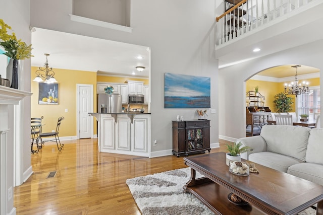 living room with light wood-type flooring, arched walkways, ornamental molding, and baseboards