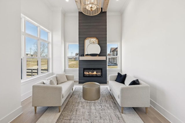 living room featuring crown molding, a large fireplace, a notable chandelier, a towering ceiling, and hardwood / wood-style floors