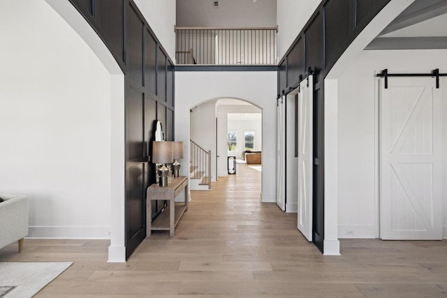 hallway featuring a barn door, light hardwood / wood-style floors, and a high ceiling