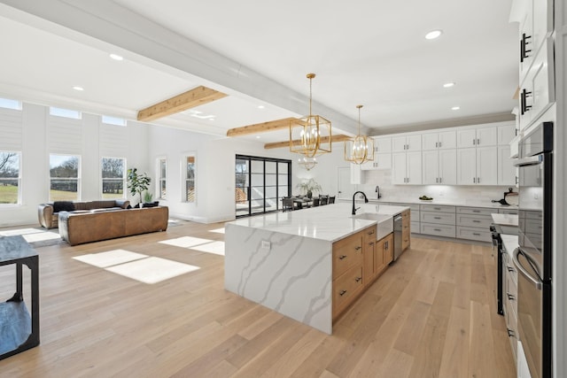 kitchen with white cabinetry, light stone counters, beam ceiling, and a spacious island