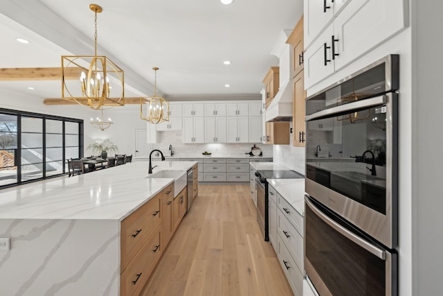 kitchen with beamed ceiling, white cabinetry, decorative light fixtures, and a large island with sink