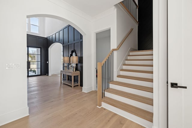 stairs with a towering ceiling, ornamental molding, and wood-type flooring