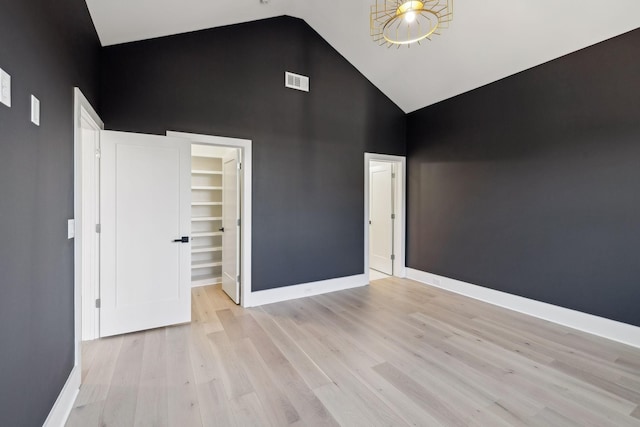 unfurnished bedroom featuring a spacious closet, high vaulted ceiling, a closet, and light wood-type flooring