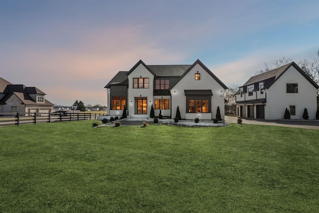 back house at dusk featuring a garage and a lawn