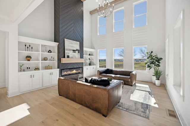 living room with a towering ceiling, light hardwood / wood-style floors, a large fireplace, and a chandelier