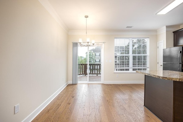 unfurnished dining area featuring a chandelier, light hardwood / wood-style floors, and crown molding