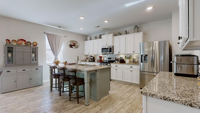 kitchen featuring a breakfast bar, a kitchen island with sink, appliances with stainless steel finishes, white cabinets, and light stone counters