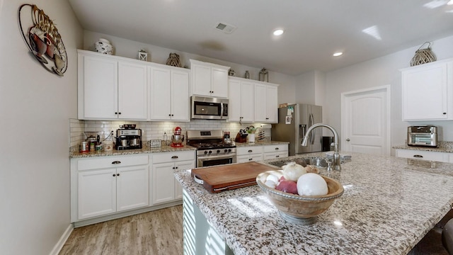 kitchen with tasteful backsplash, white cabinetry, a kitchen island with sink, stainless steel appliances, and light stone counters