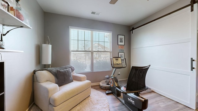 sitting room featuring ceiling fan, a barn door, and wood-type flooring