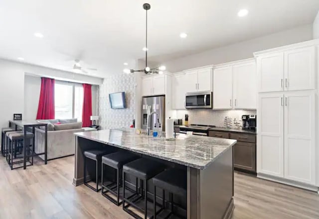 kitchen featuring a kitchen bar, stainless steel appliances, ceiling fan, light hardwood / wood-style floors, and white cabinetry