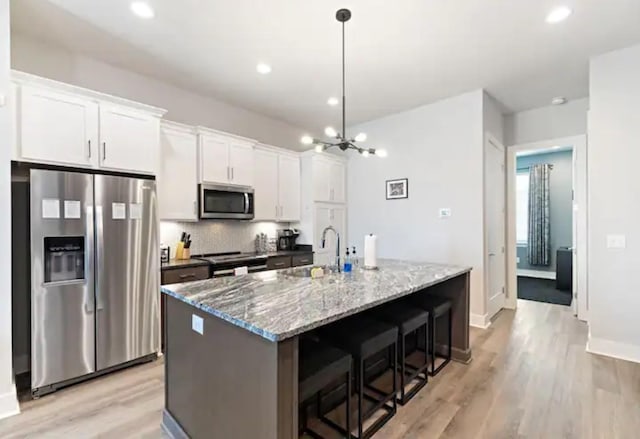 kitchen with white cabinetry, sink, stainless steel appliances, dark stone countertops, and a kitchen island with sink