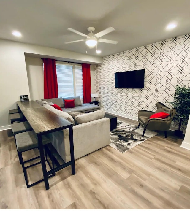 living area featuring wallpapered walls, an accent wall, baseboards, and wood finished floors