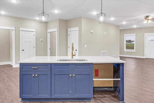 kitchen featuring a center island with sink, blue cabinetry, sink, and hanging light fixtures