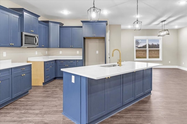 kitchen featuring pendant lighting, sink, an island with sink, and dark wood-type flooring