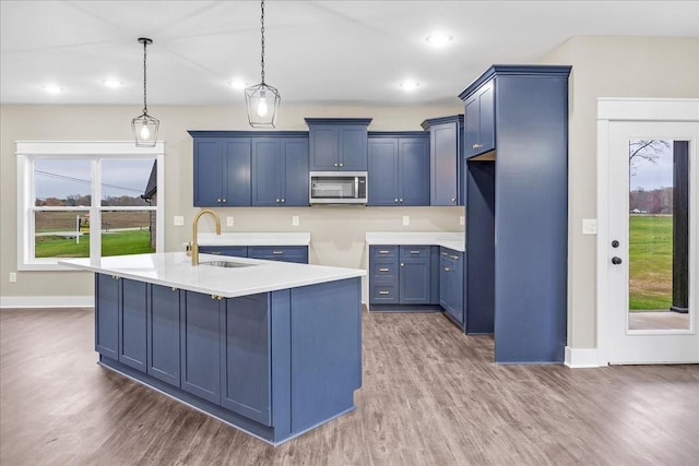 kitchen featuring dark hardwood / wood-style flooring, blue cabinets, a kitchen island with sink, sink, and hanging light fixtures