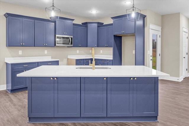 kitchen featuring a center island with sink, sink, hanging light fixtures, and dark wood-type flooring