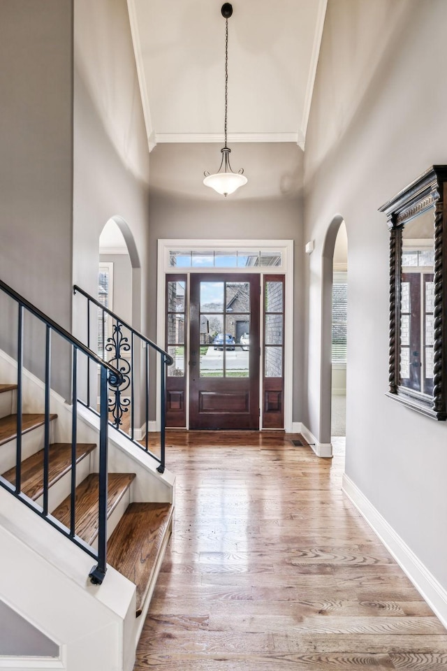 foyer entrance with hardwood / wood-style floors, a towering ceiling, and crown molding