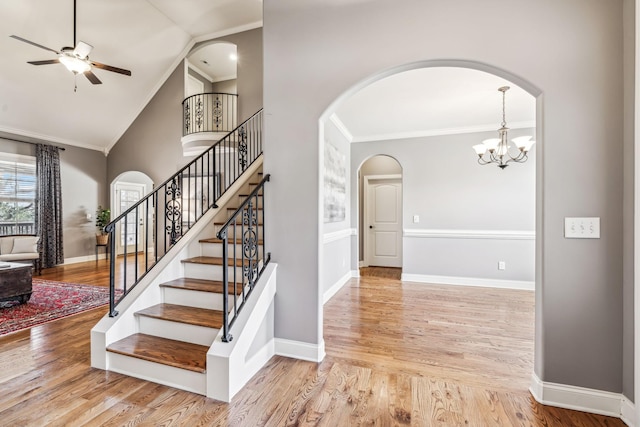 staircase with ceiling fan with notable chandelier, wood-type flooring, ornamental molding, and vaulted ceiling