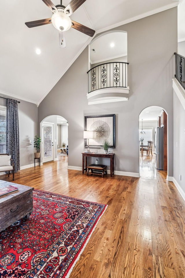 living room featuring high vaulted ceiling, crown molding, ceiling fan, light wood-type flooring, and a wealth of natural light