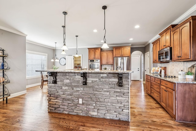 kitchen featuring backsplash, stainless steel appliances, a large island with sink, hanging light fixtures, and a breakfast bar area