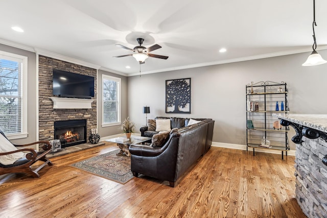 living room featuring wood-type flooring, a stone fireplace, ceiling fan, and crown molding