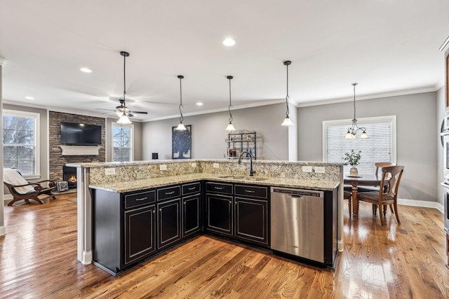 kitchen with sink, a stone fireplace, stainless steel dishwasher, a large island with sink, and pendant lighting