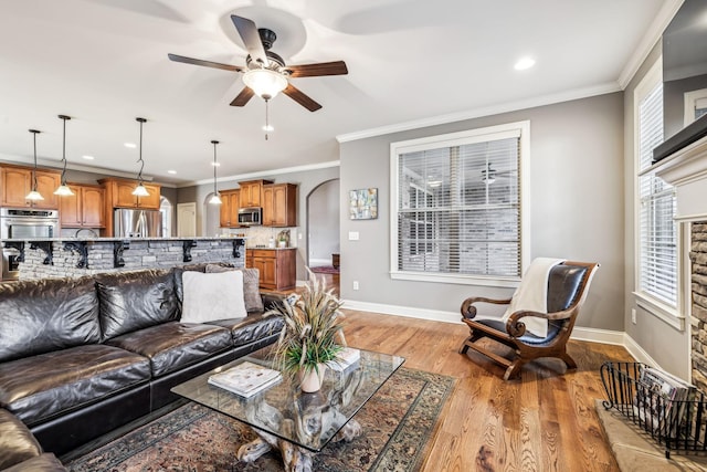 living room featuring a stone fireplace, crown molding, ceiling fan, and light hardwood / wood-style floors