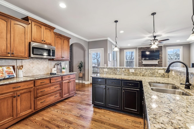 kitchen featuring light stone countertops, ornamental molding, sink, pendant lighting, and light hardwood / wood-style flooring